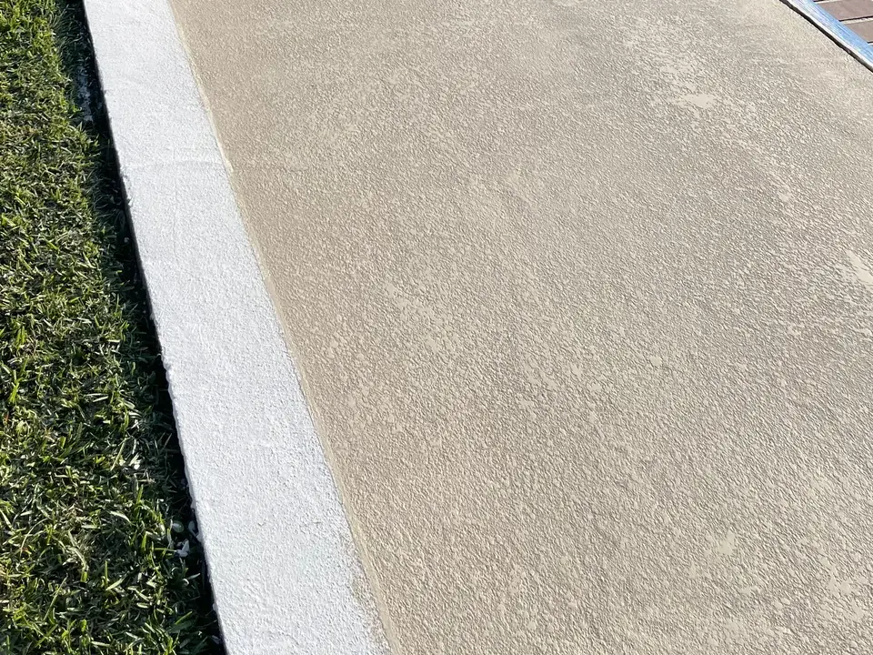Close view of a light knockdown-textured pool deck beside the lawn edge.