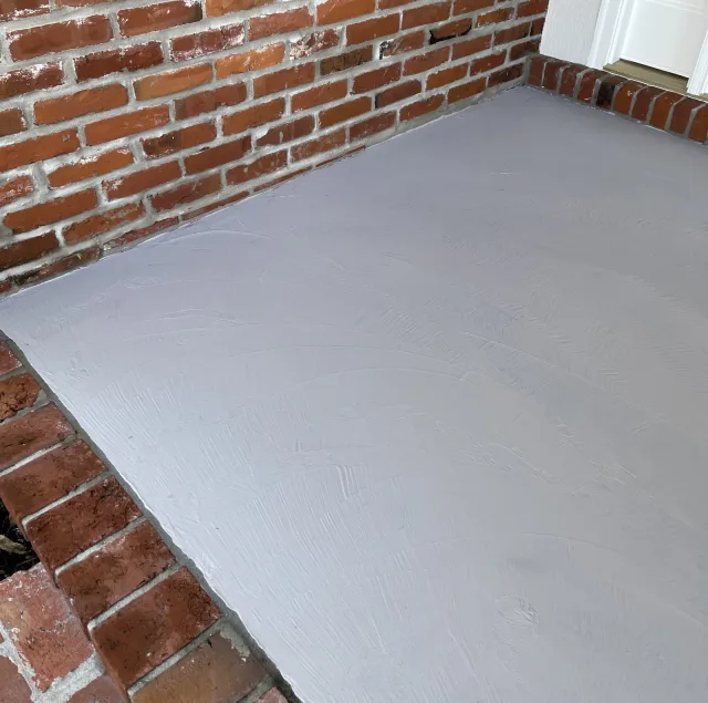 Gray porch surface at the same brick corner during resurfacing, before the brick pattern.