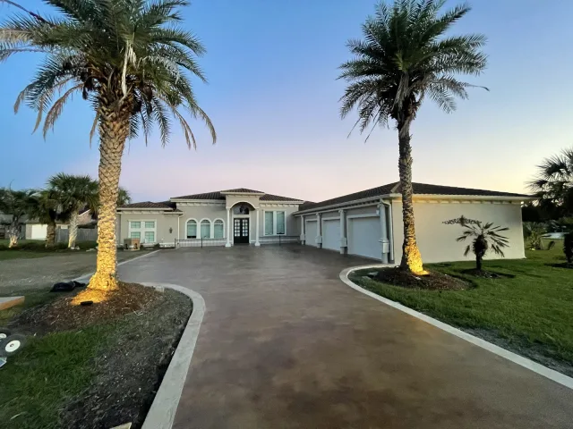 The same driveway at dusk with the curved cream border and illuminated palms.