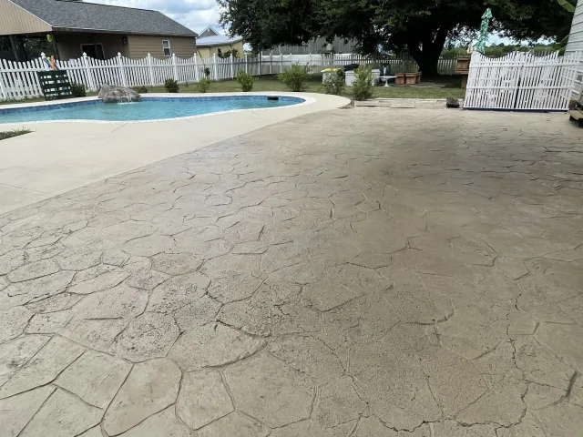 Existing worn stamped stone-pattern pool deck before resurfacing.