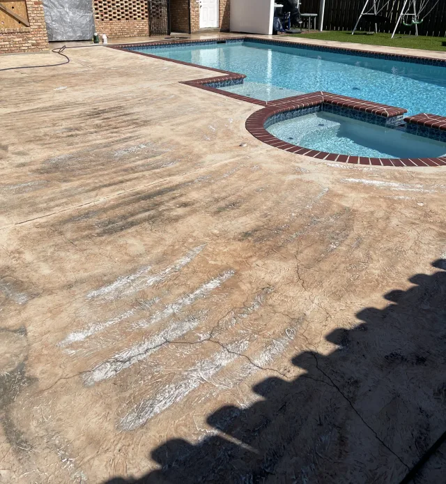 Worn tan deck and surface streaks around the same pool and spa before resurfacing.