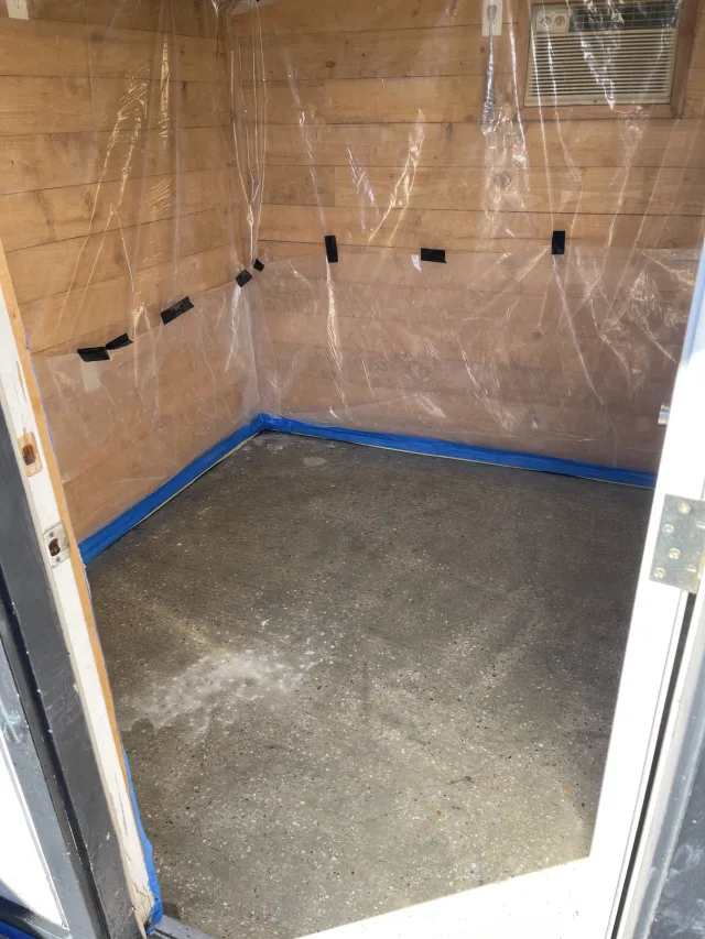 Bare concrete slab with walls masked in plastic before staining.